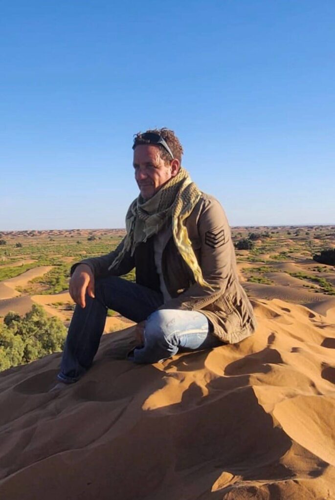 Abdel A,ik assis sur une dune dans le désert avec le regard pensil